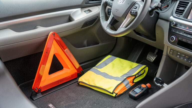 Triangle de signalisation, gilet haute visibilité et éthylotest posés sur le tapis de voiture, vus en lumière naturelle, style photo documentaire.